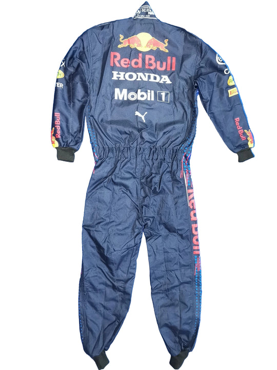 A dark navy Red Bull Racing one-piece jumpsuit with sponsor logos including Red Bull, Honda, Mobil 1, Puma, and Castore, laid flat on a crinkled blue background.