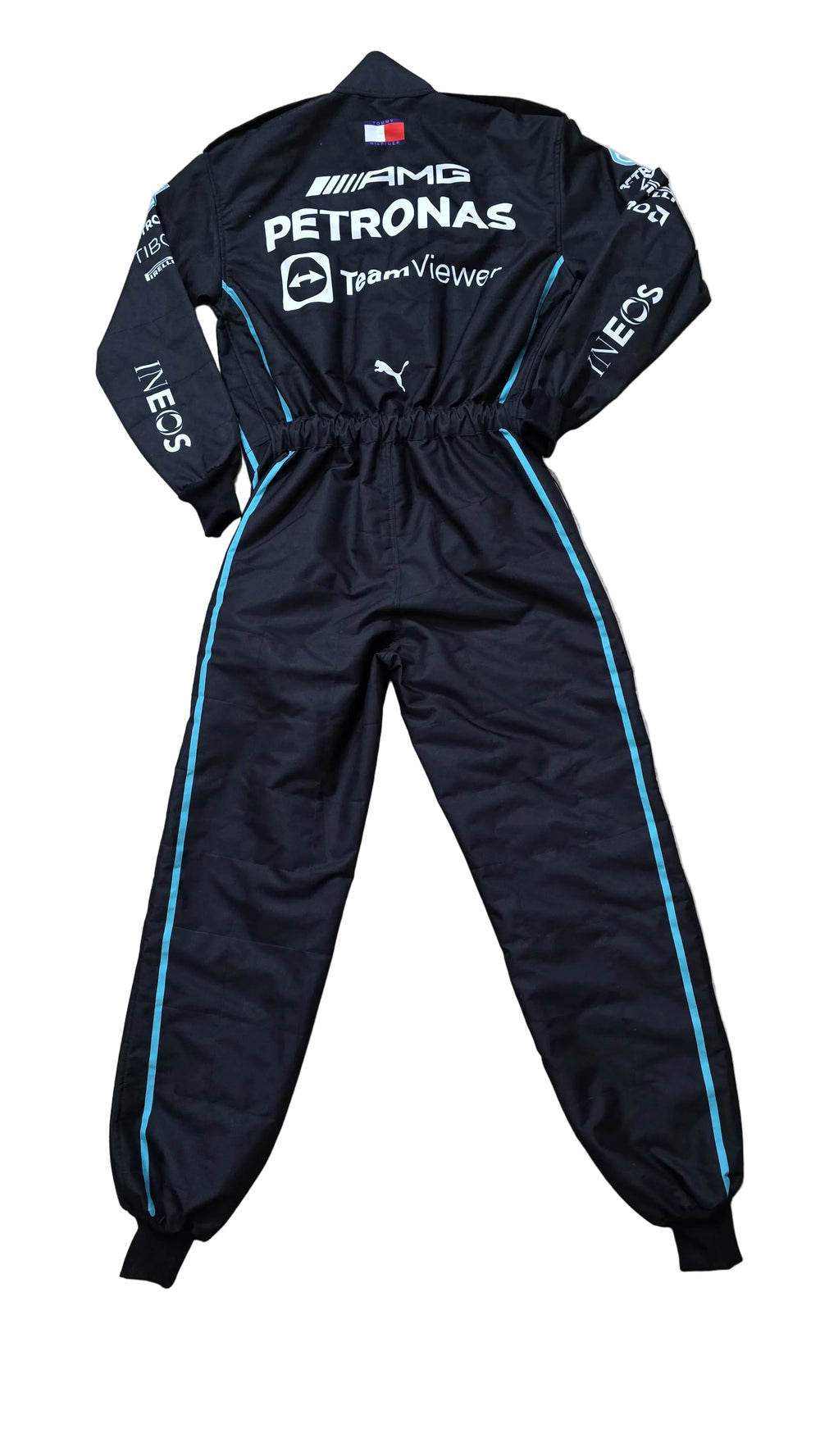 A black Puma Mercedes-AMG racing tracksuit with white and light blue sponsor logos and side stripes, laid flat on a beige marble floor.