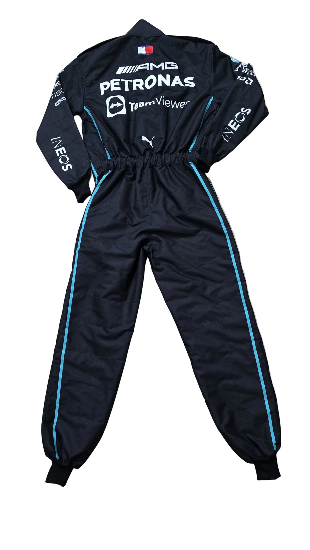 A black Puma Mercedes-AMG racing tracksuit with white and light blue sponsor logos and side stripes, laid flat on a beige marble floor.