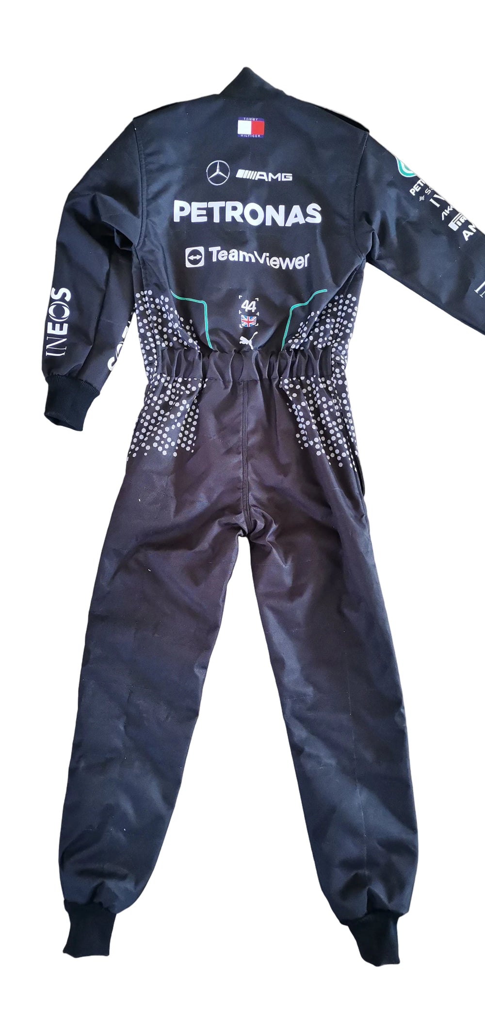 A black Mercedes-AMG Petronas Team F1 racing suit laid flat on a beige tiled floor. The suit features white sponsor logos, green accents, and a small French flag patch on the back neck.