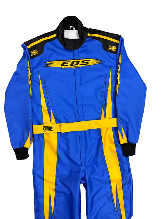 A blue and yellow EDS Racing OMP racing suit laid flat on a gray marble tile floor. The suit features a bright blue body with bold yellow graphic stripes, a yellow chest logo, a yellow waist belt, and black shoulder and cuff accents.