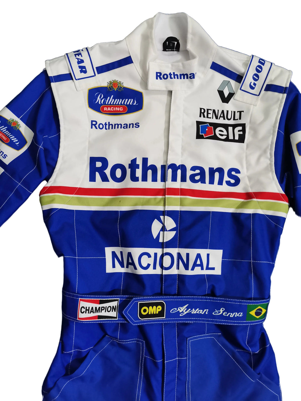 A blue and white racing suit laid flat on a blue fabric background, featuring prominent Rothmans, Renault, and Elf sponsor logos, with 'NACIONAL' across the chest and 'Champion' and 'Ayrton Senna' patches.
