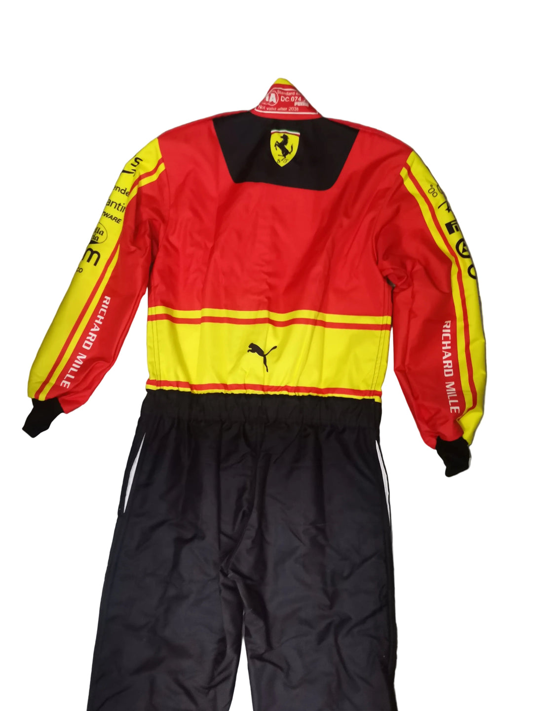 A red and yellow Puma racing jacket with black pants, laid flat on a gray marble-patterned floor. The jacket features the Ferrari shield logo on the back neck, Puma logos on the chest, and 'RICHARD MILLE' printed down the sleeves.