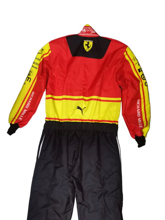 A red and yellow Puma racing jacket with black pants, laid flat on a gray marble-patterned floor. The jacket features the Ferrari shield logo on the back neck, Puma logos on the chest, and 'RICHARD MILLE' printed down the sleeves.