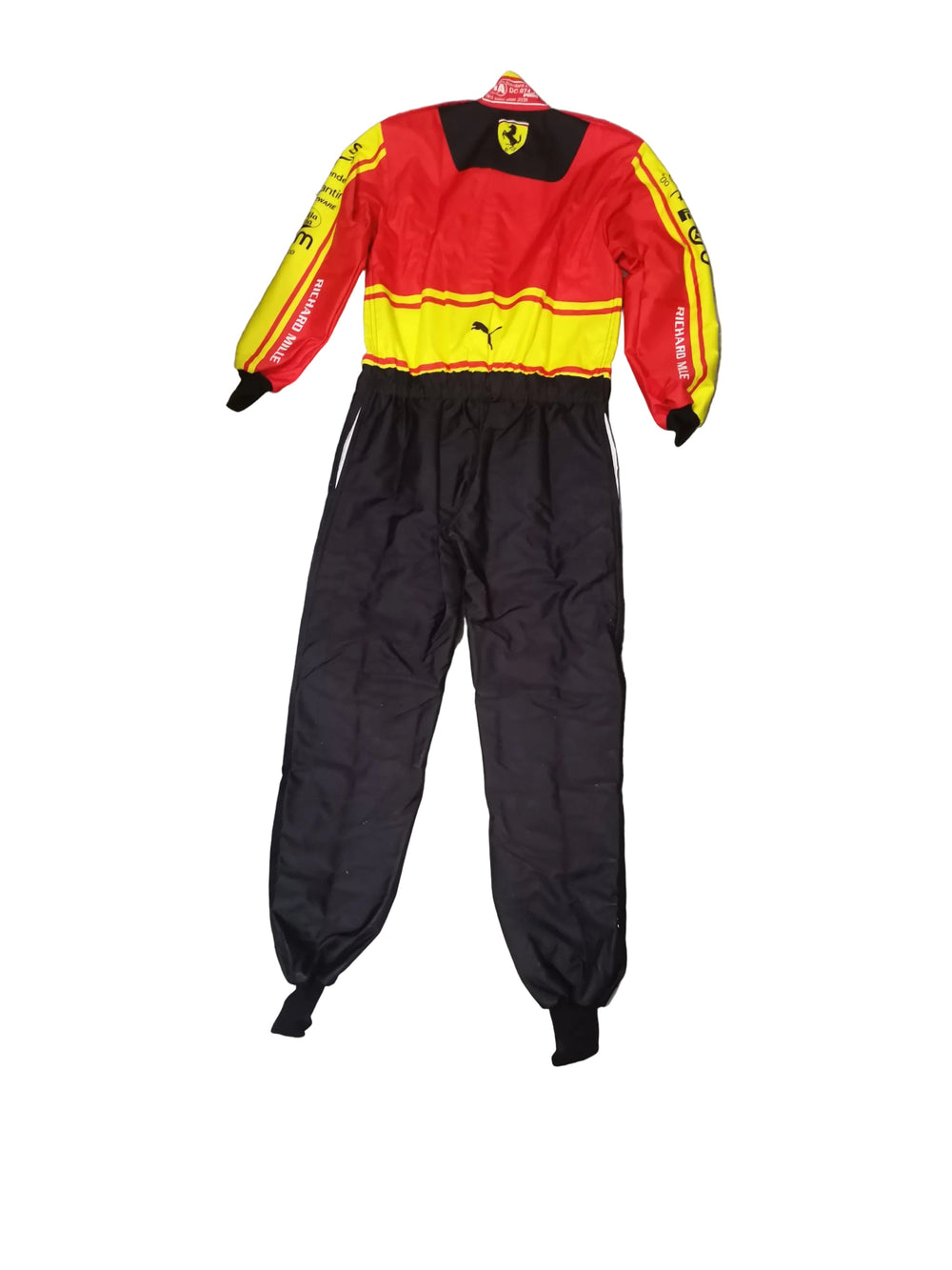 A red, yellow, and black Ferrari racing suit laid flat on a gray marble-patterned floor. The suit features the Ferrari logo on the chest and shoulders, Puma branding on the waist, and 'Scuderia Ferrari' text on the sleeves.