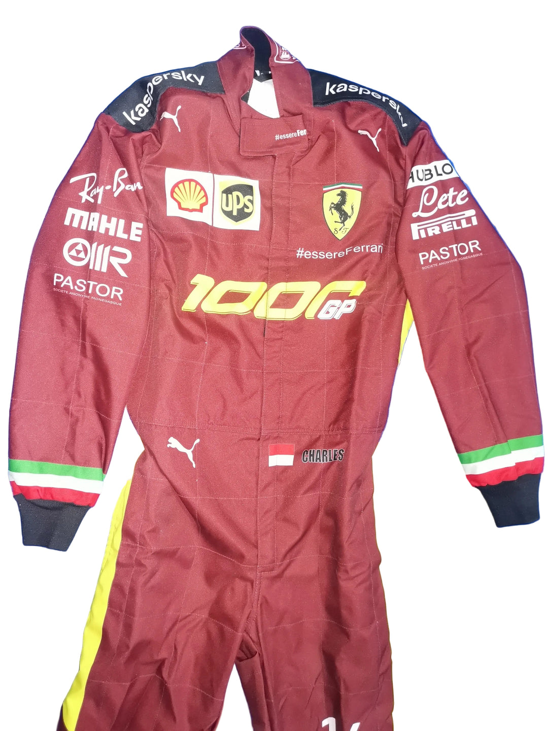 A maroon Ferrari racing suit with yellow and green side stripes, laid flat on a blue background. The suit features multiple sponsor logos including Puma, Kaspersky, Shell, UPS, Mahle, Pastor, and others, with the Ferrari shield on the chest.