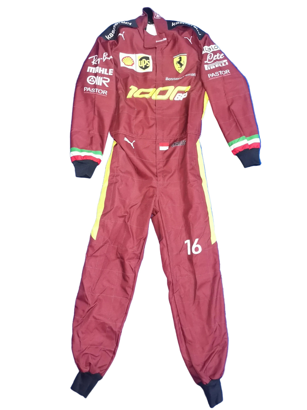A maroon Ferrari F1 racing suit with yellow and white side stripes, laid flat on a crinkled blue background. The suit features various sponsor logos including Shell, Puma, and Castore, and the number 16 on the left leg.