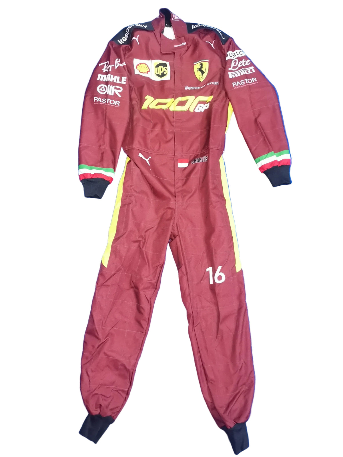 A maroon Ferrari F1 racing suit with yellow and white side stripes, laid flat on a crinkled blue background. The suit features various sponsor logos including Shell, Puma, and Castore, and the number 16 on the left leg.
