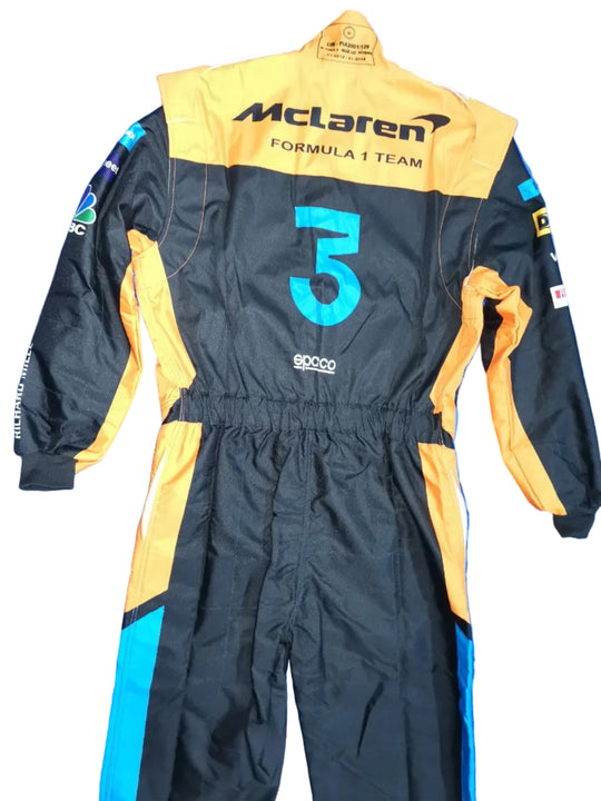 A black and yellow McLaren Formula 1 Team racing suit with the number 5, laid flat on a crinkled blue background. Visible brands include McLaren, Formula 1, Sparco, and Haas.