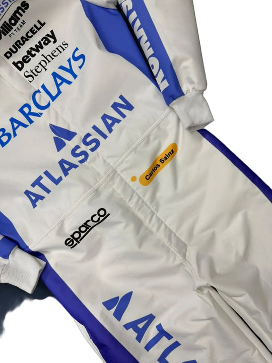 A close-up of a white racing suit with blue and purple panels, featuring sponsor logos including Barclays, Atlassian, Sparco, Williams, and Duracell.