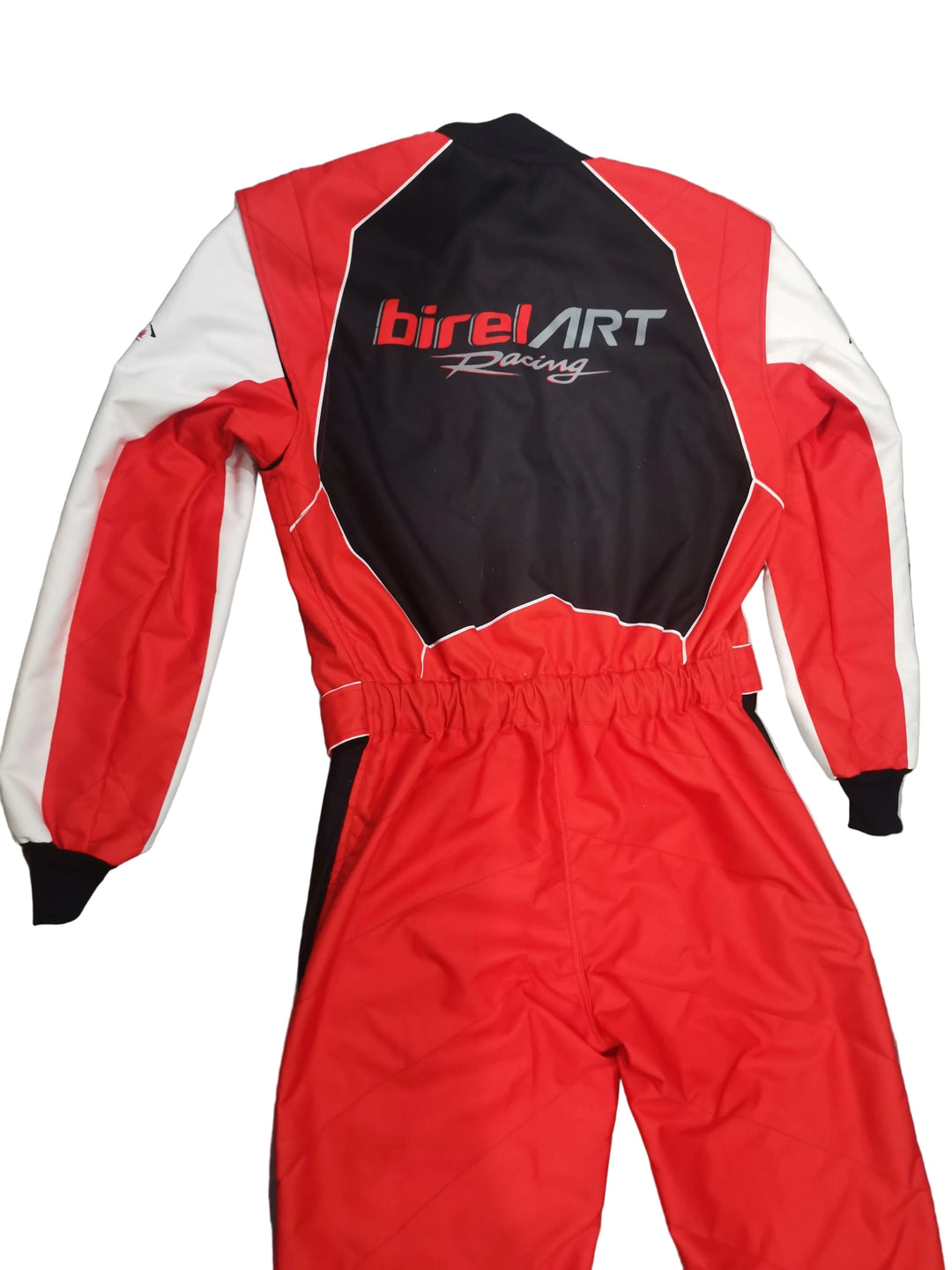 A red, black, and white BirelArt Racing one-piece racing suit laid flat on a gray marble-patterned floor, showing the back view with the brand logo.