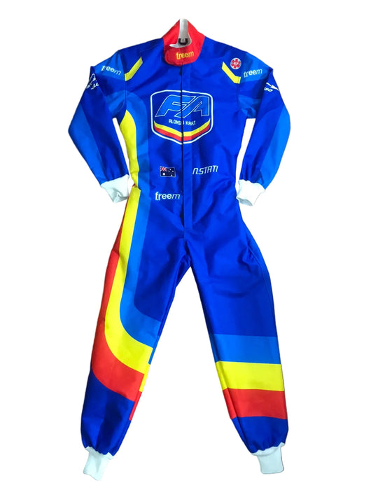 A blue FIA racing one-piece suit with yellow and red graphic stripes, laid flat on a brown wooden floor. The suit features the FIA World of F1 logo on the chest, 'freem' branding on the thigh, and 'NSRAN' on the arm.