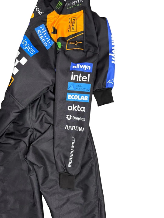 A black racing suit with multiple sponsor logos, including Allwyn, Intel, Ecolab, Okta, Dropbox, and Arrow, laid flat on a gray marble floor.