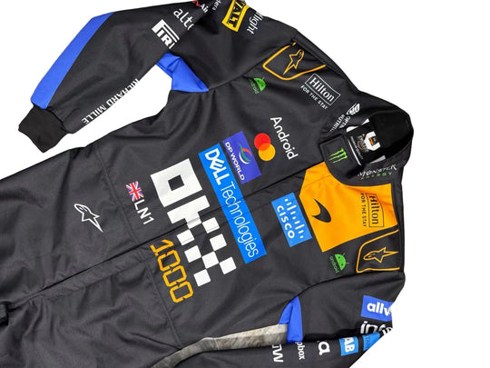 A black Alpinestars F1 team racing suit with various sponsor logos, including Dell Technologies, Android, and Mastercard, laid flat on a gray marble surface.