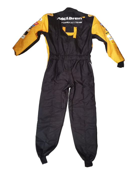 A black and yellow McLaren Formula 1 Team racing suit laid flat on a gray marble-patterned floor. The suit features the McLaren logo and 'FORMULA 1 TEAM' on the back, with the number 4 printed in yellow.