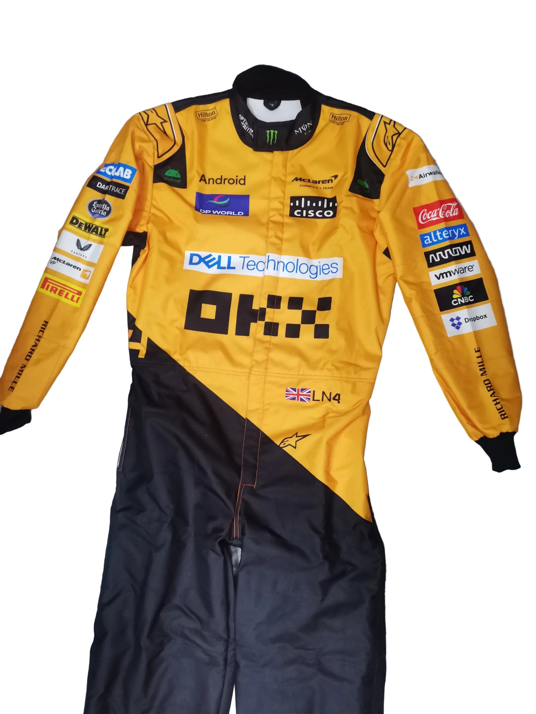 A yellow and black racing suit with multiple sponsor logos, laid flat on a gray marble tile floor. A brown sandal is partially visible at the bottom right corner.