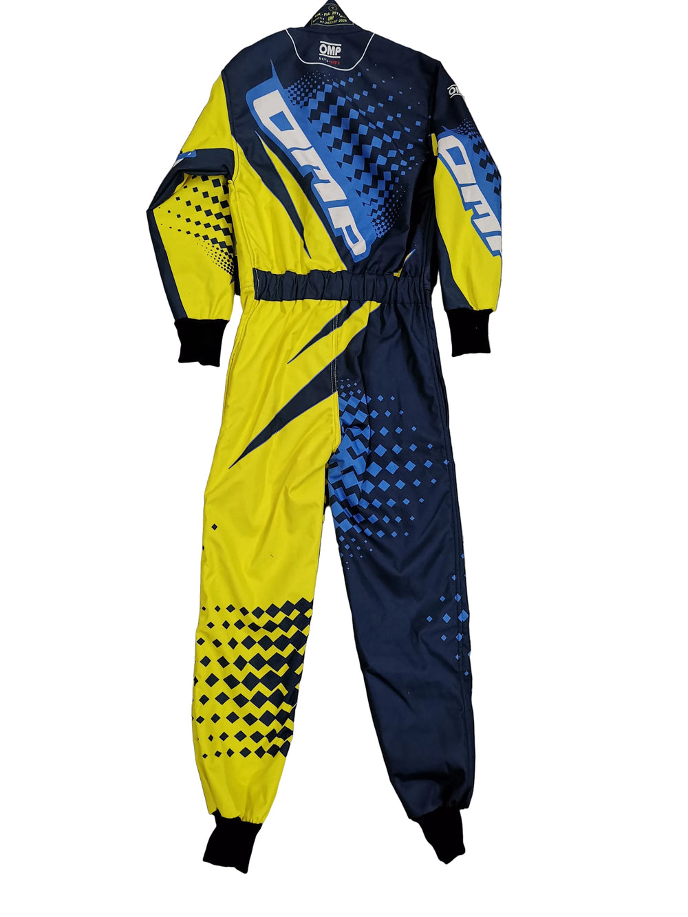 A long-sleeve racing suit laid flat on a gray marble-patterned tile floor. The suit features a bold color-blocked design with bright yellow, dark navy blue, and blue geometric halftone patterns, and the word 'OMNI' printed in large white letters across the chest and sleeves.