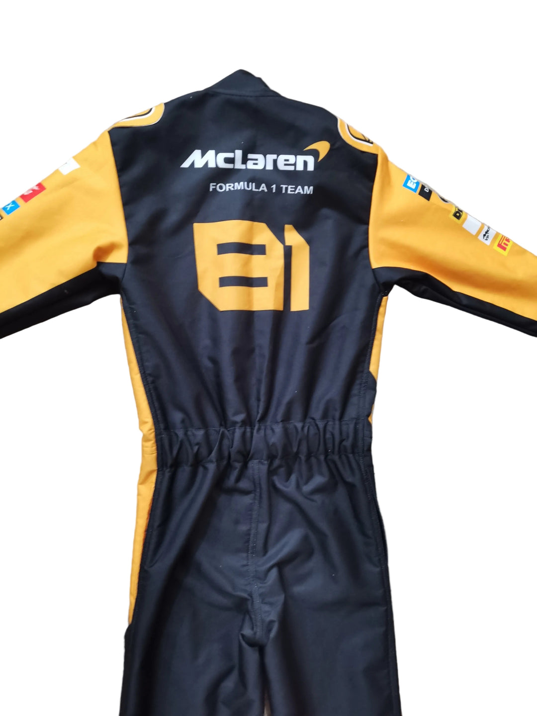 A black and yellow long-sleeve racing suit laid flat on a beige stone-textured surface, shown from the back with 'McLaren Formula 1 Team' and the number 81 printed on it.