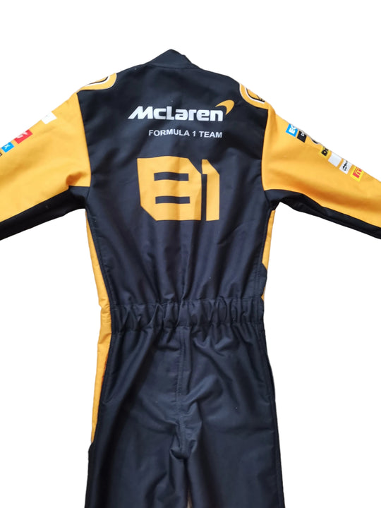 A black and yellow long-sleeve racing suit laid flat on a beige stone-textured surface, shown from the back with 'McLaren Formula 1 Team' and the number 81 printed on it.