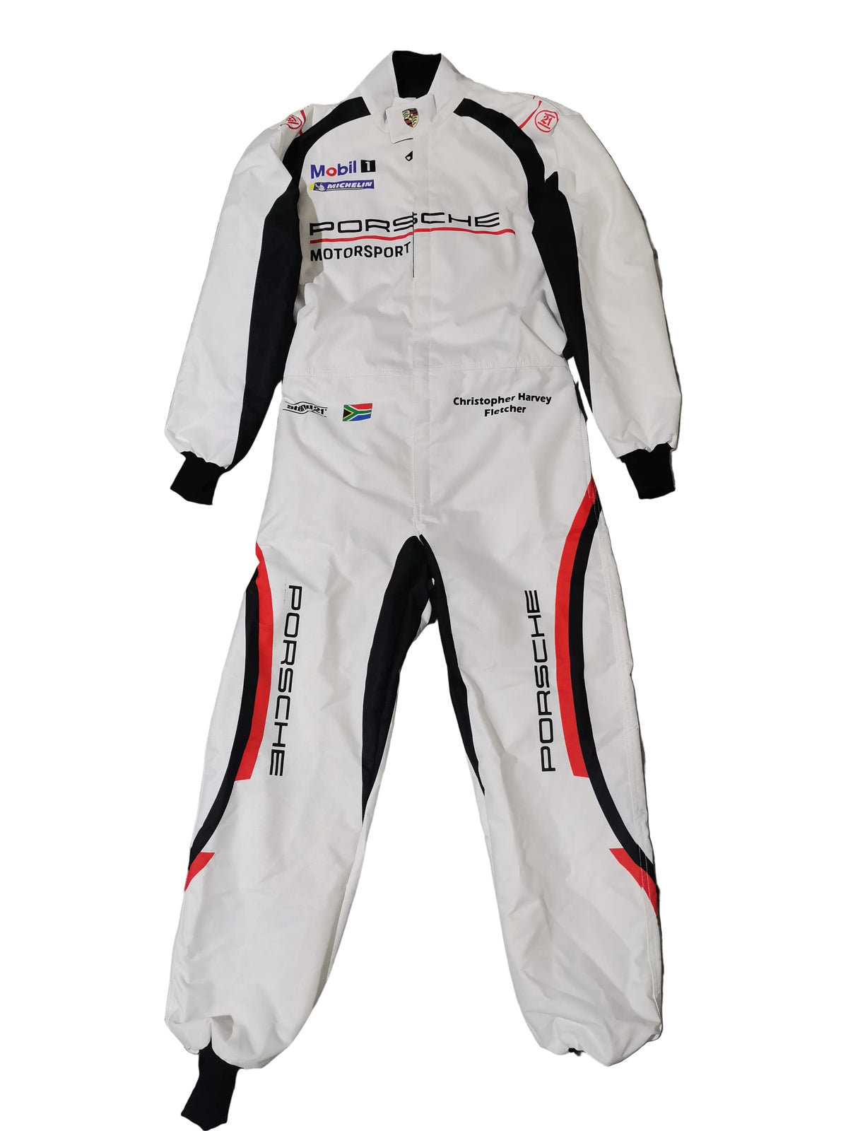 A white Porsche Motorsport racing suit with black and red side panels, laid flat on a gray marble-patterned tile floor. The suit features various sponsor logos including Mobil 1, Mobil 1 Racing, and Christian de Sousa Racing.
