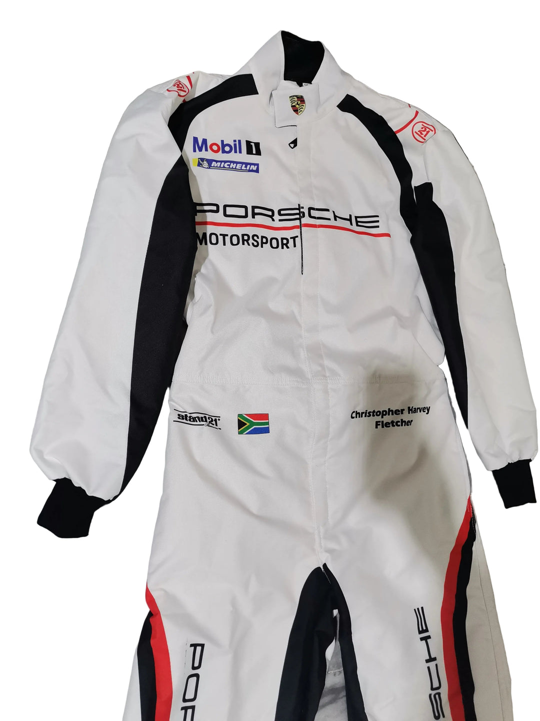A white Porsche Motorsport racing suit with black and red accents, featuring sponsor logos like Mobil 1 and Pirelli, laid flat on a gray marble-patterned floor.