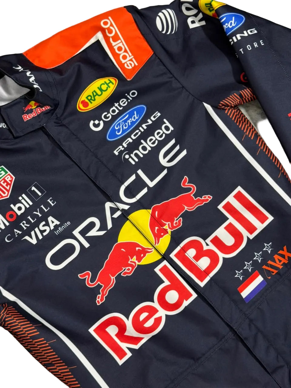 A close-up of a dark navy Red Bull Racing team jacket or suit cover with multiple sponsor logos including Oracle, Red Bull, Mobil 1, Visa, and Ford, laid flat on a gray surface.
